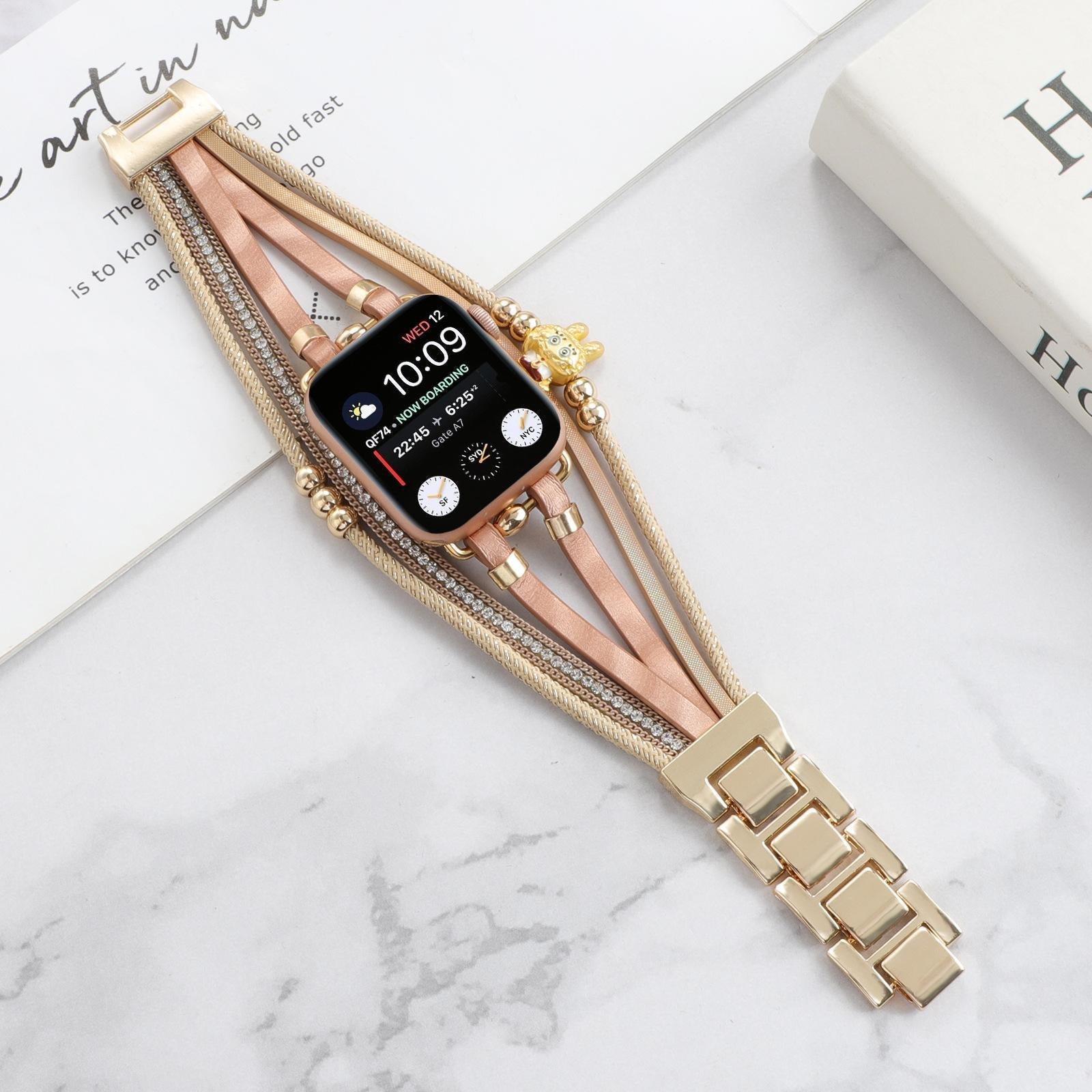 Bracelet Apple Watch doré avec fines lanières roses, perles dorées, strass brillants et breloque ours teddy élégante.