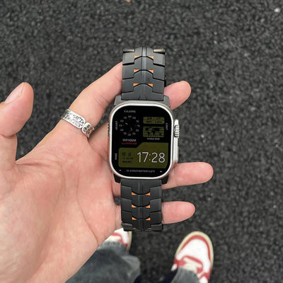 Bracelet connecté Apple Ultra en titane massif noir mat avec maillons ajourés et détails orange, fermeture boucle sécurisée,