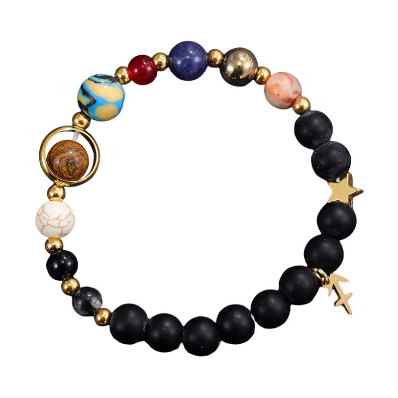 Bracelet en perles noires mates et pierres naturelles colorées avec charms étoiles dorées et planète en métal doré.