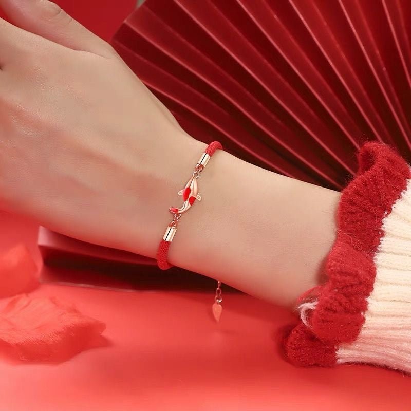 Bracelet fin en fil rouge ciré avec pendentif carpe koï en métal argenté porté au poignet féminin.