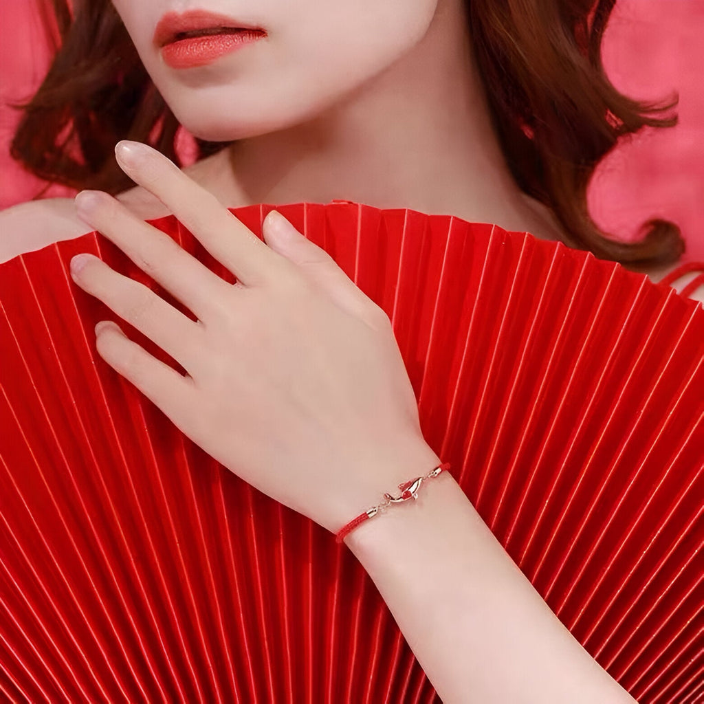 Bracelet rouge en fil ciré avec pendentif Carpe Koï porté au poignet féminin sur fond rouge plissé.