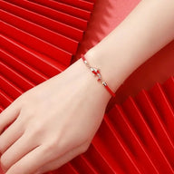 Bracelet rouge en fil ciré avec pendentif carpe koï argenté, porté au poignet féminin.