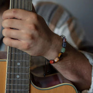 Bracelet Solva en corde avec perles de pierres naturelles multicolores sur poignet masculin jouant de la guitare.
