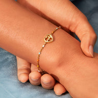 Bracelet fin en or avec pendentif cœur et battement de cœur, porté au poignet féminin.