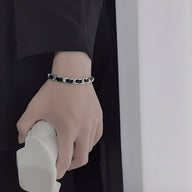 Bracelet homme noir en titane et cuir tressé sur poignet avec manches sombres.