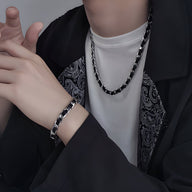 Bracelet homme en cuir noir tressé avec maillons en titane gris, style moderne.