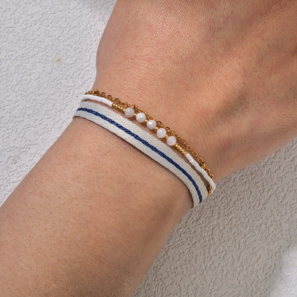 Bracelet bohème multirangs avec ruban rayé blanc et bleu, perles blanches nacrées, chaîne dorée fine, fermoir mousqueton.