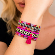 Bracelet boho chic multi-couches en tissu ethnique rose et rouge, pompon fuchsia, strass et chaînes dorées, fermoir aimanté.