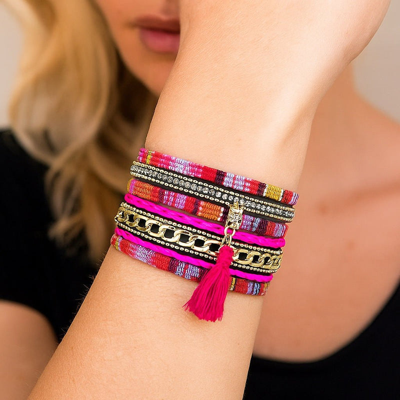 Bracelet boho chic multi-couches en tissu ethnique rose et rouge, pompon fuchsia, strass et chaînes dorées, fermoir aimanté.