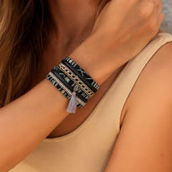Bracelet boho multi-couches tressé noir avec pompon gris, tissu ethnique et strass argentés, fermoir aimanté.