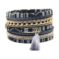 Bracelet multi-couches noir et blanc en tissu ethnique tressé, chaîne dorée, strass et pompon gris avec fermoir aimanté.