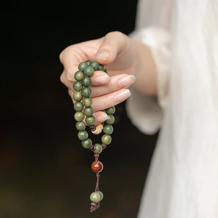 Bracelet bouddha perles vertes en bois de santal avec breloques rouges et bois clair sur fil brun.