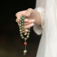 Bracelet bouddha perles vertes en bois de santal avec breloques rouges et bois clair sur fil brun.