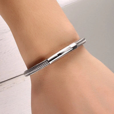 Bracelet câble en acier inoxydable argenté avec fermoir lisse porté au poignet.