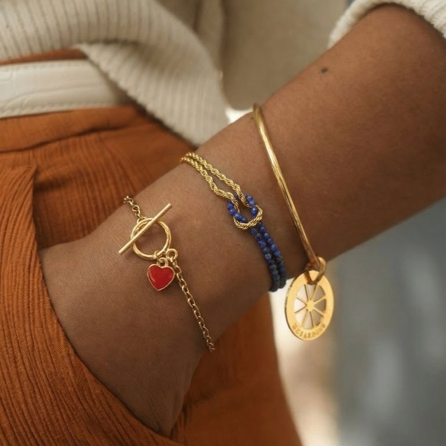 Bracelet chaîne torsadée dorée avec pendentif médaille gravée, perles naturelles rouges et bleues, style élégant et délicat.