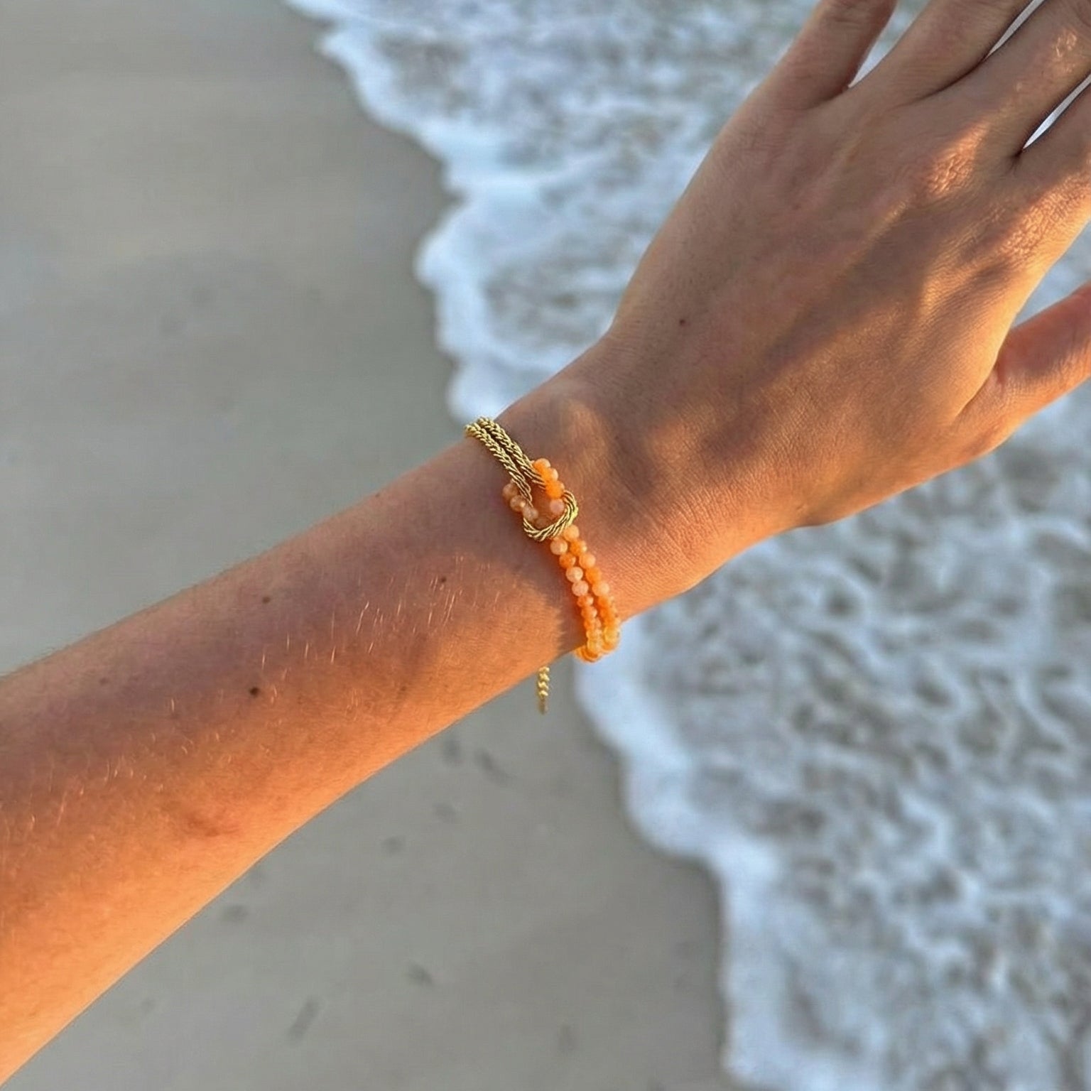 Bracelet chaîne torsadée dorée avec perles multicolores en pierres naturelles porté au poignet féminin sur fond de plage.