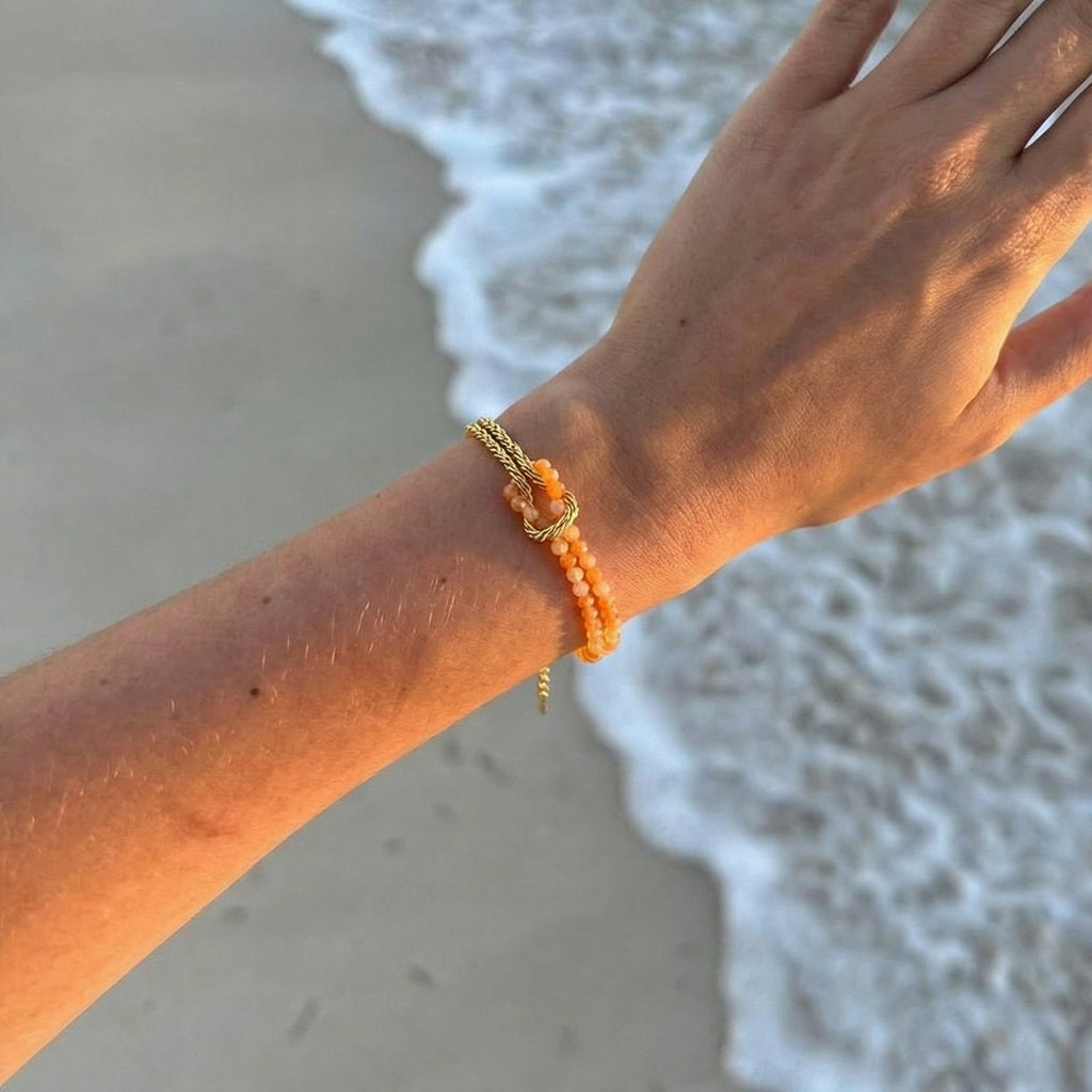 Bracelet chaîne torsadée dorée avec perles multicolores en pierres naturelles porté au poignet féminin sur fond de plage.