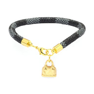 Bracelet noir en microfibre aspect cuir avec breloque sac à main dorée et fermoir plaqué or.