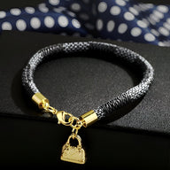 Bracelet charm sac à main en microfibre noire, fermoir et pendentif dorés, modèle Yirelle.