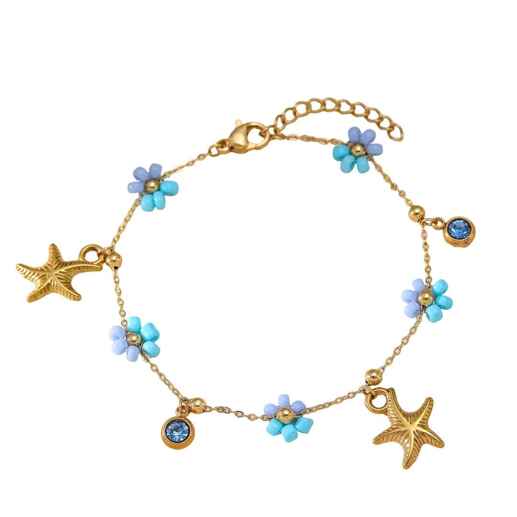 Bracelet doré en acier inoxydable avec charms étoiles de mer, fleurs bleues et cristaux brillants.