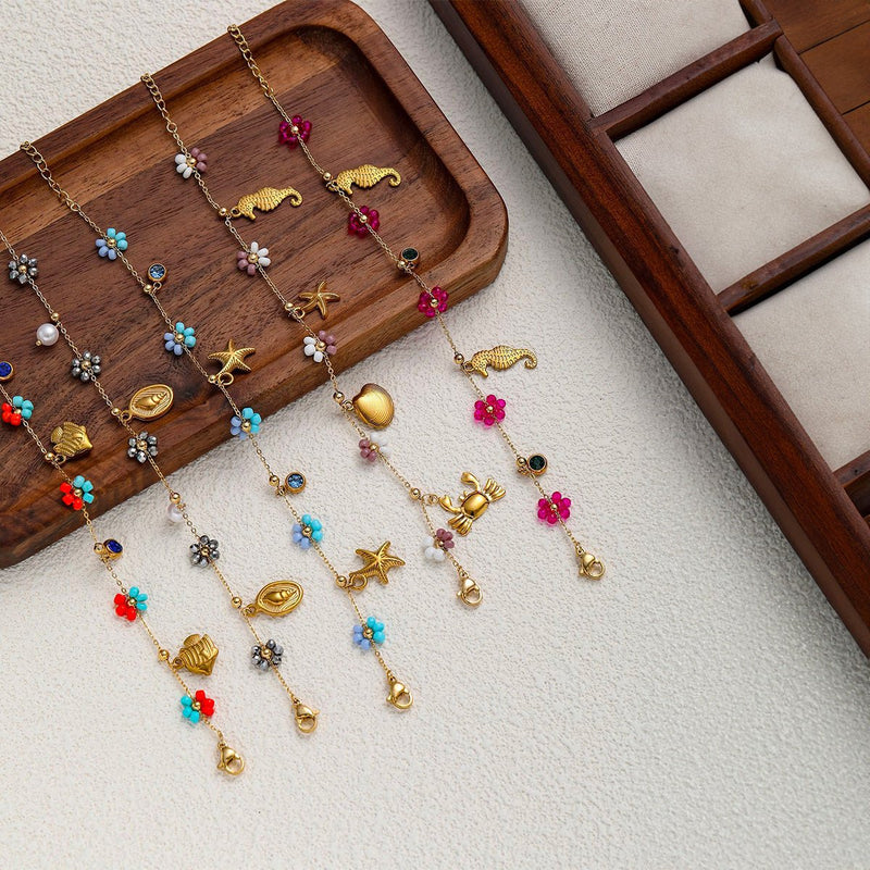 Set de bracelets charms en acier inoxydable doré avec pendentifs soleil, cœur, étoile et fleurs colorées sur chaîne fine.