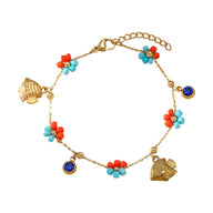 Bracelet doré en acier inoxydable avec charms soleil, coquillages et perles bleu clair et rouge corail.