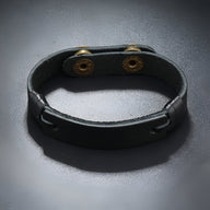 Bracelet homme en cuir noir effet vintage avec double pression métallique dorée.