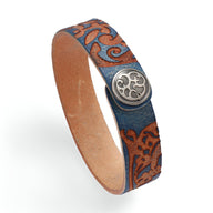 Bracelet en cuir bleu avec motif floral gravé et fermoir métallique circulaire décoré.