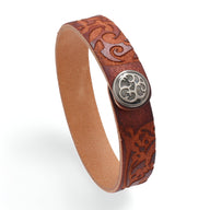Bracelet en cuir cognac avec motif floral gravé et bouton métallique décoratif argenté.