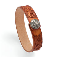 Bracelet en cuir cognac avec motif floral gravé et bouton métallique circulaire gravé.