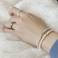 Bracelet chic double rang de perles d'imitation blanches porté avec une bague assortie sur main féminine.