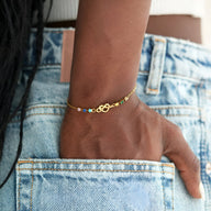 Bracelet en or avec cœurs emmêlés et perles colorées sur poignet femme.