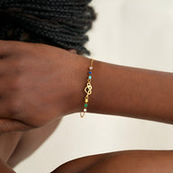 Bracelet femme en or avec pendentif cœur emmêlé et petites pierres colorées sur chaîne fine.