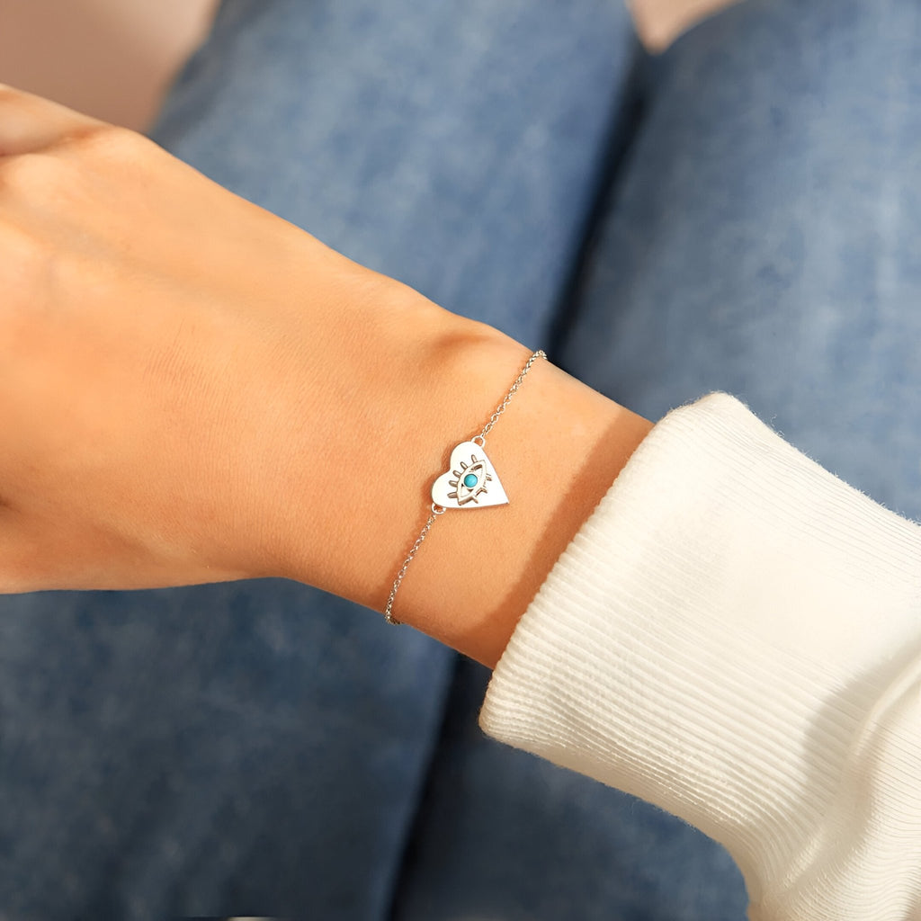 Bracelet fin en argent sterling avec pendentif cœur incrusté d'un œil bleu, porté au poignet féminin.
