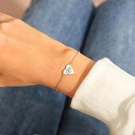 Bracelet fin en argent sterling avec pendentif cœur incrusté d'un œil bleu, porté au poignet féminin.