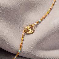 Bracelet en or avec pendentif cœur incrusté d'une rose et chaîne fine ornée de petites perles colorées.