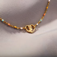 Bracelet en or avec pendentif cœur ajouré et rose stylisée, chaîne fine ornée de perles colorées.