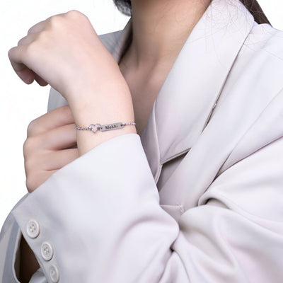 Bracelet argenté en acier inoxydable avec pendentif cœur délicat, porté sur poignet féminin.