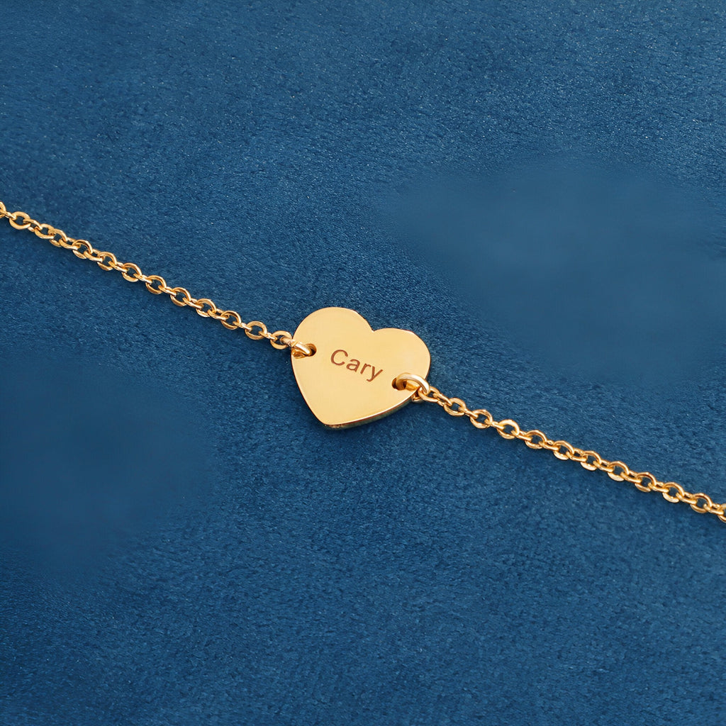 Bracelet fin en acier inoxydable doré avec pendentif cœur gravé « Cary » sur fond bleu.