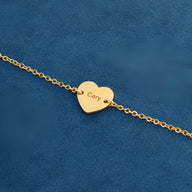 Bracelet fin en acier inoxydable doré avec pendentif cœur gravé « Cary » sur fond bleu.