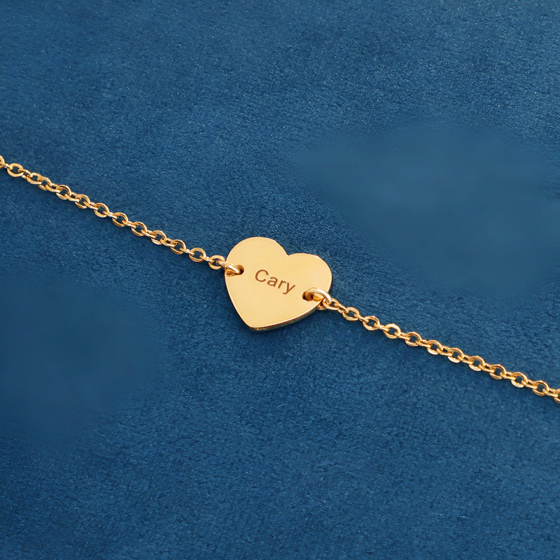 Bracelet fin en acier inoxydable doré avec pendentif cœur gravé « Cary » sur fond bleu.