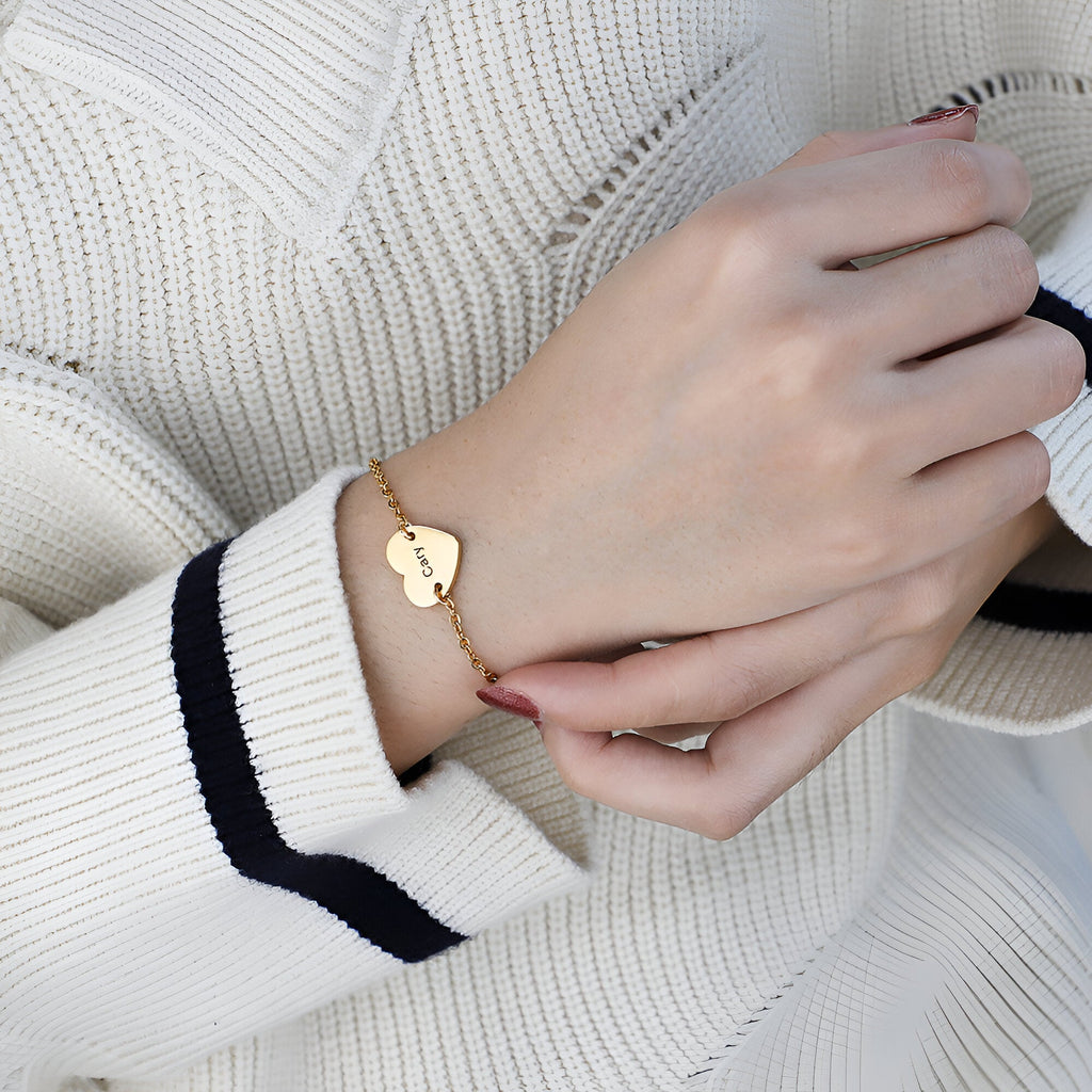 Bracelet en acier inoxydable doré avec cœur personnalisé gravé, porté sur poignet féminin.