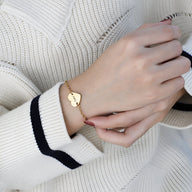 Bracelet en acier inoxydable doré avec cœur personnalisé gravé, porté sur poignet féminin.