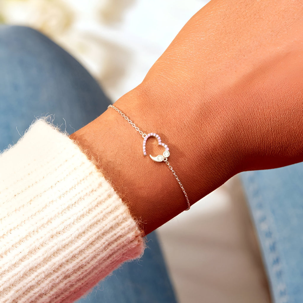 Bracelet fin en argent sterling avec pendentif cœur délicat ajouré sur poignet féminin.