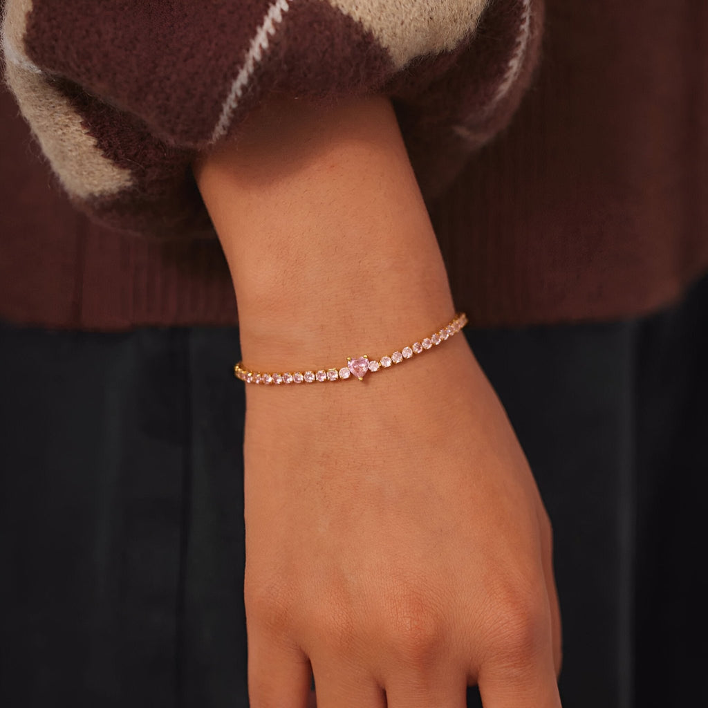 Bracelet fin en argent sterling doré rose avec un petit cœur et zircons brillants sur poignet féminin.