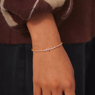 Bracelet fin en argent sterling doré rose avec un petit cœur et zircons brillants sur poignet féminin.