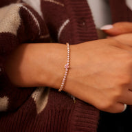 Bracelet fin en argent sterling rosé avec cœur serti de zirconium rose porté au poignet.