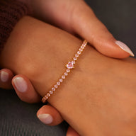 Bracelet fin en argent sterling rosé avec cœur central serti de zirconium rose sur poignet féminin.
