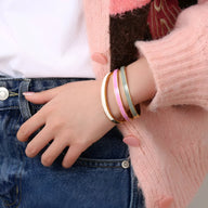 Bracelet jonc en titane plaqué or avec émail rose pâle porté avec gilet rose et jean bleu.