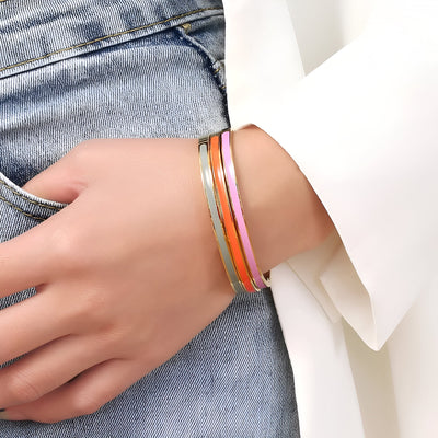 Bracelet jonc plaqué or avec émail coloré orange et rose porté sur poignet féminin avec jean bleu et manche blanche.